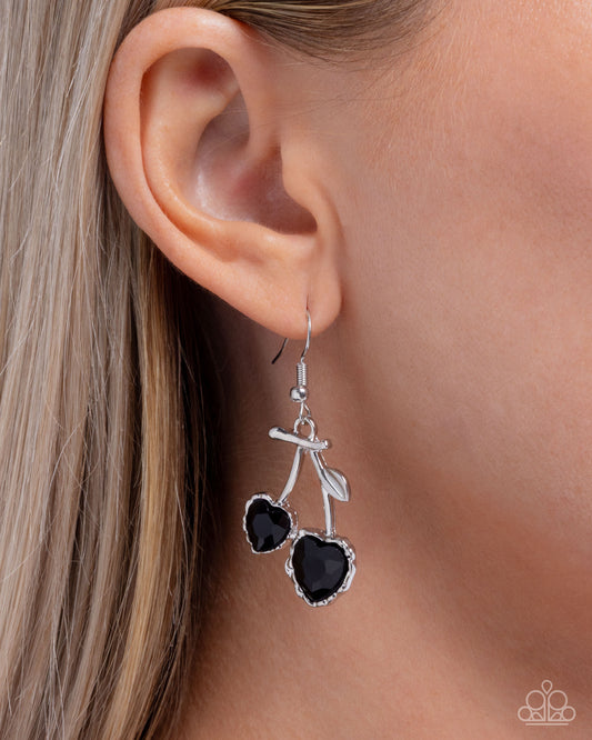 Silver earrings with black heart-shaped stones worn by a person with blonde hair.
