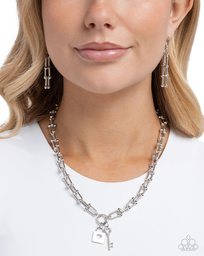 Woman wearing a silver necklace with a heart key charm on a white background