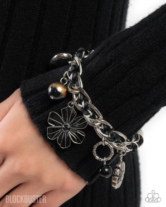 Close-up of a hand wearing a silver charm bracelet with black accents against a black background.