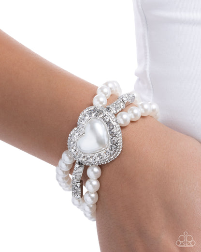 Pearl bracelet with heart-shaped center on a wrist against a white background