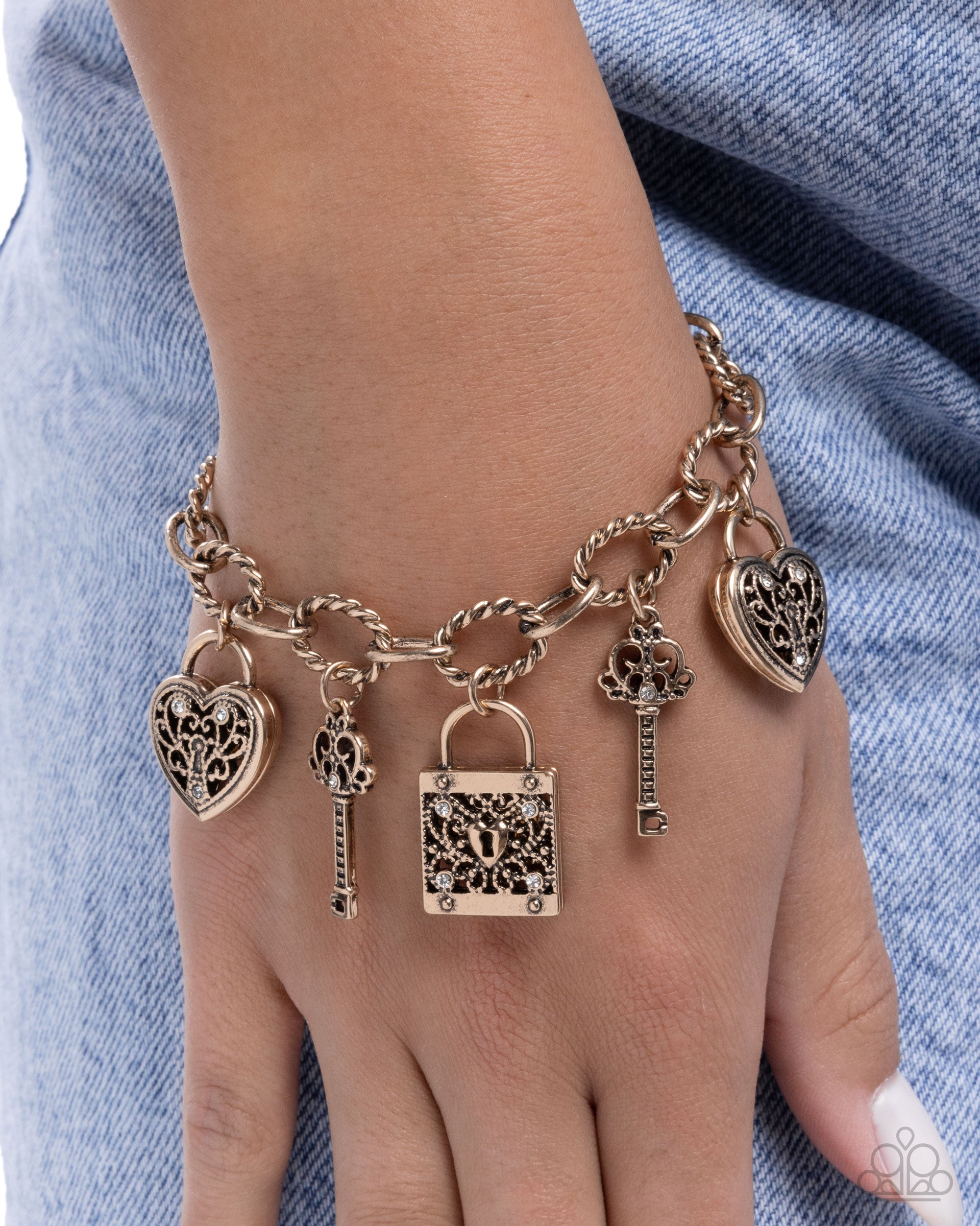 Bracelet with heart, key, and lock charms on a wrist against a denim background