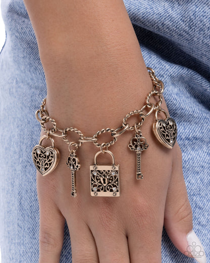 Bracelet with heart, key, and lock charms on a wrist against a denim background