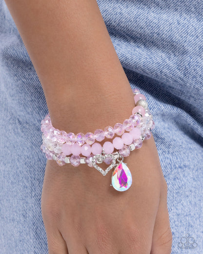 Pink beaded bracelet with a heart and teardrop charm on a wrist against a denim background
