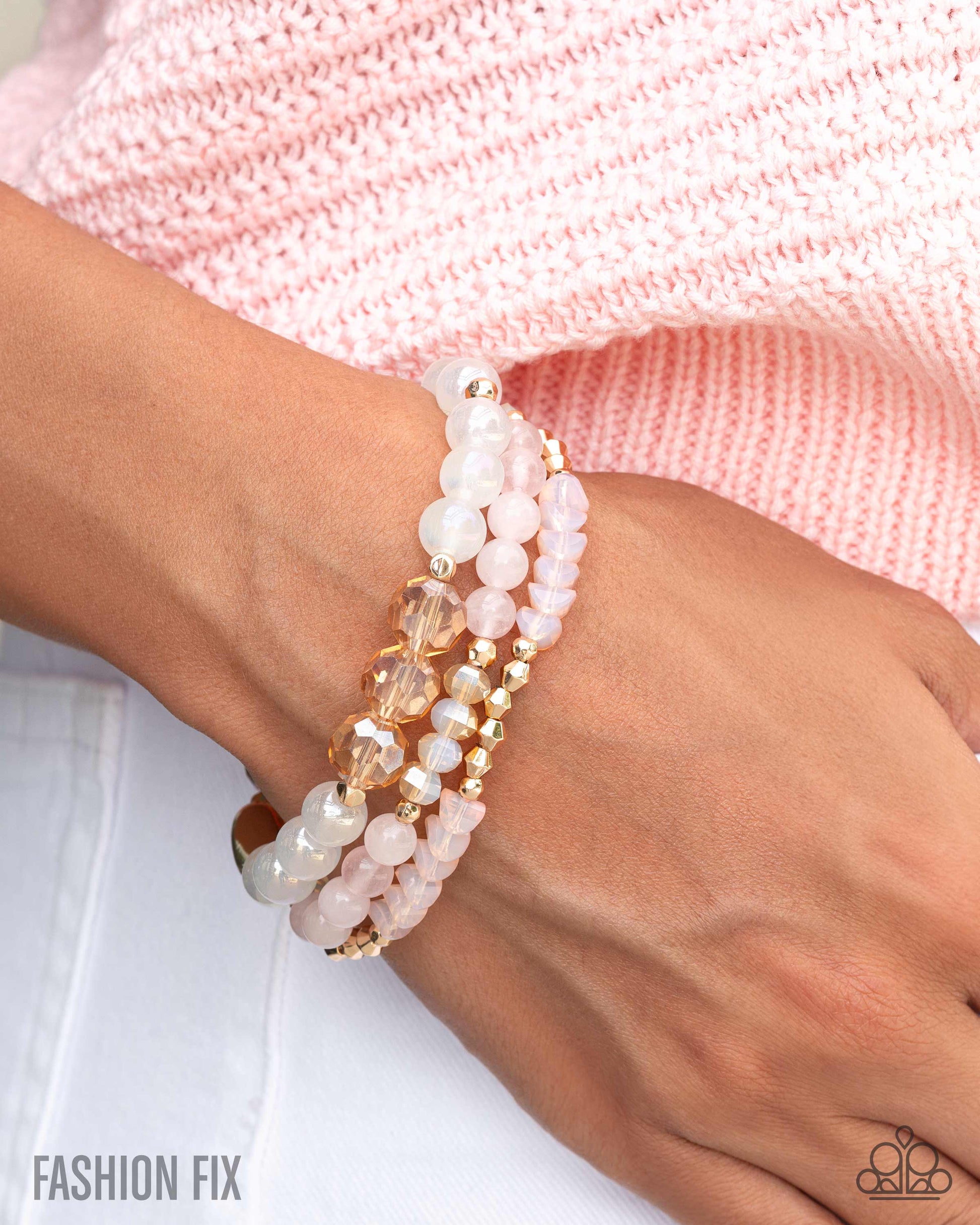 Stack of beaded bracelets on a wrist with a pink textured background