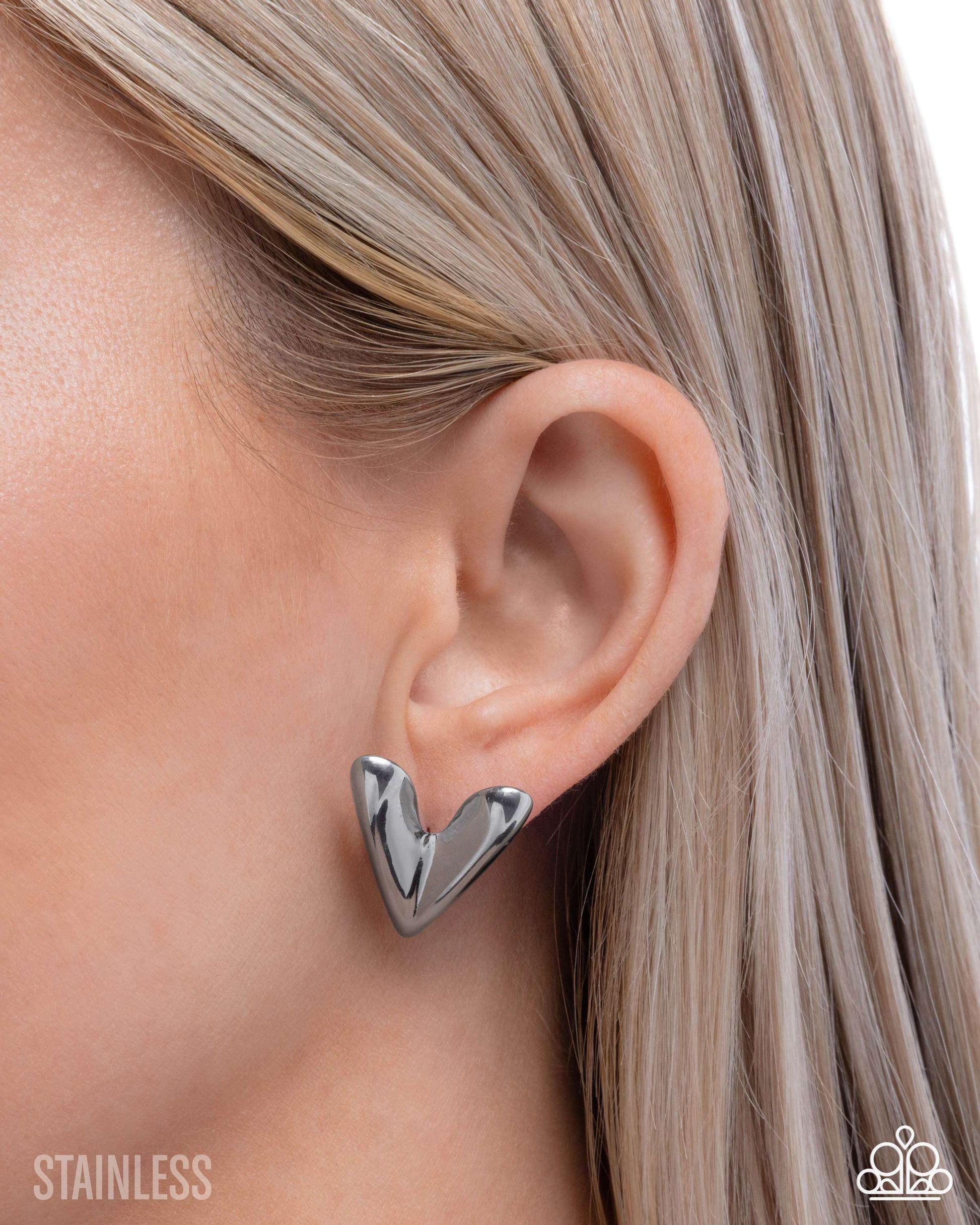 Silver heart-shaped earring worn by a person with blonde hair.