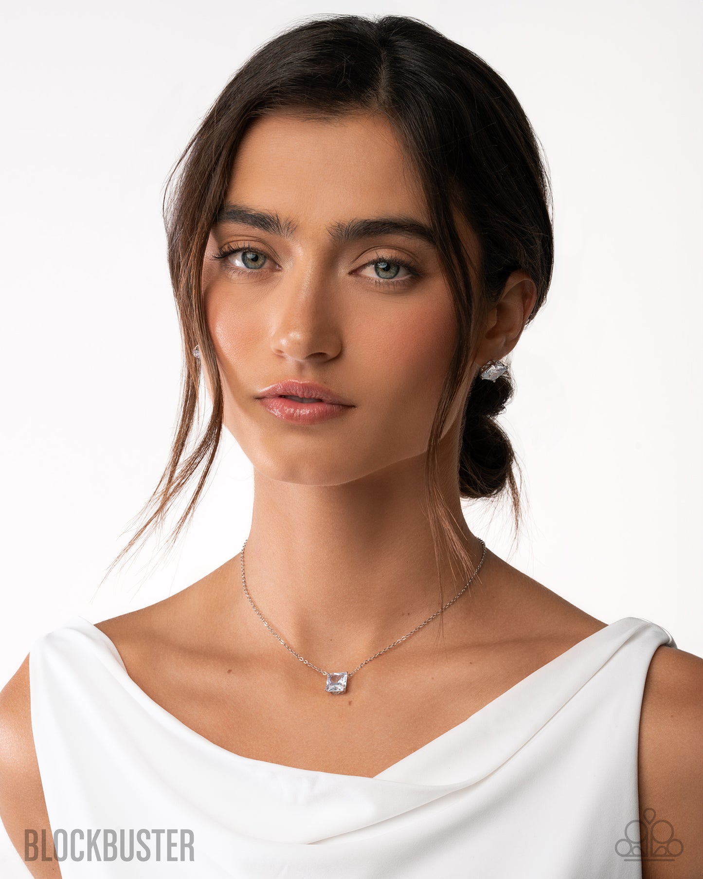 Woman wearing a white top and necklace on a plain background