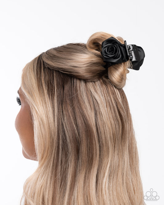 Blonde hair styled in an updo with a black flower accessory on a white background