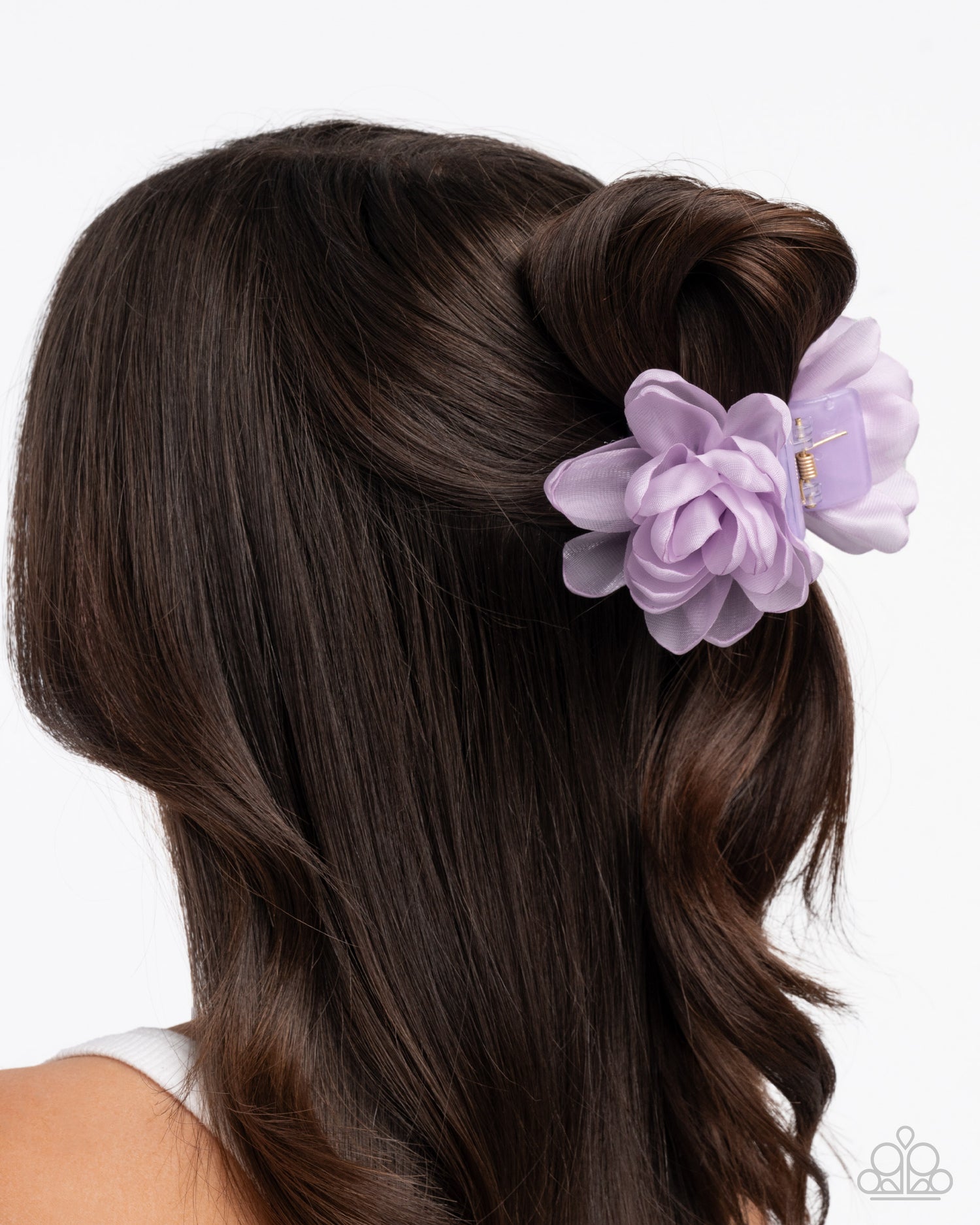 Woman with brown hair styled in an updo with a lavender flower accessory on a white background