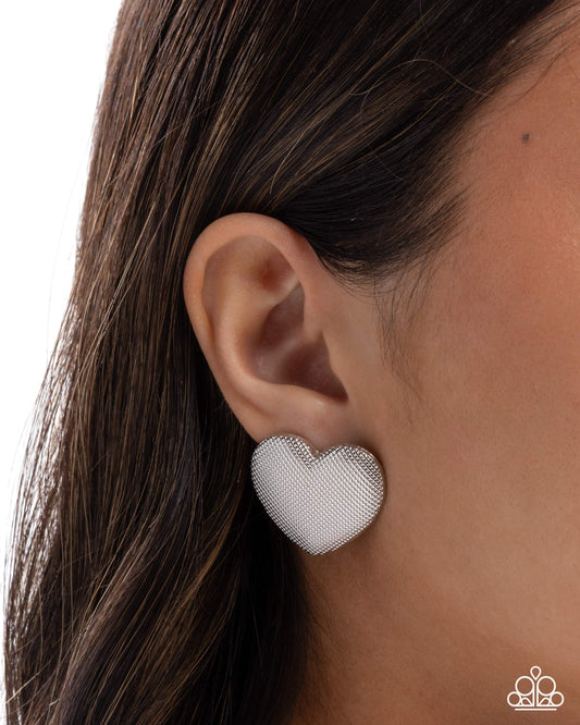 Heart-shaped silver earring worn by a person with dark hair.