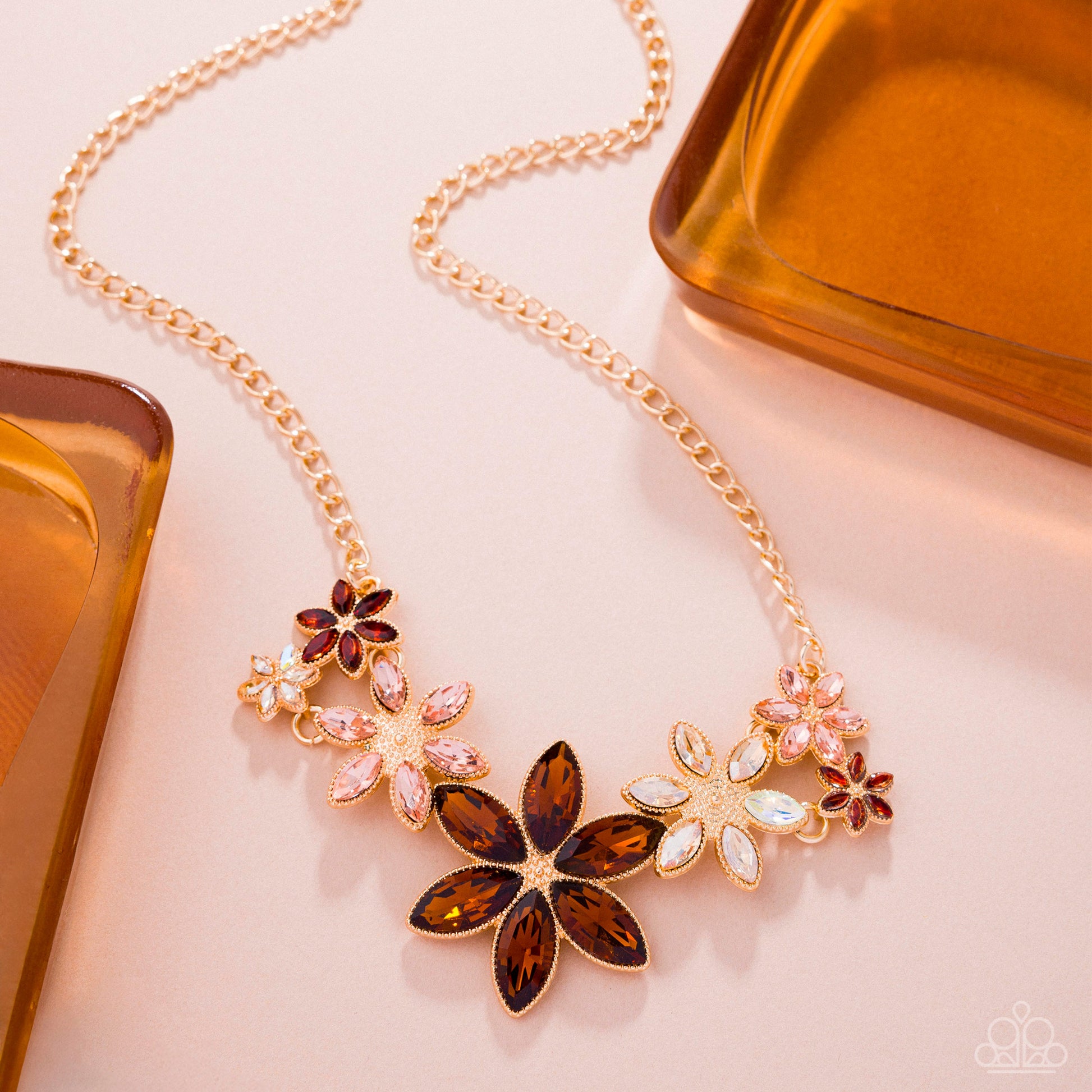 Gold necklace with floral pendant on a light pink background