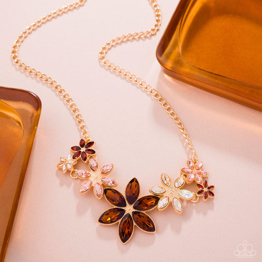 Gold necklace with floral pendant on a light pink background
