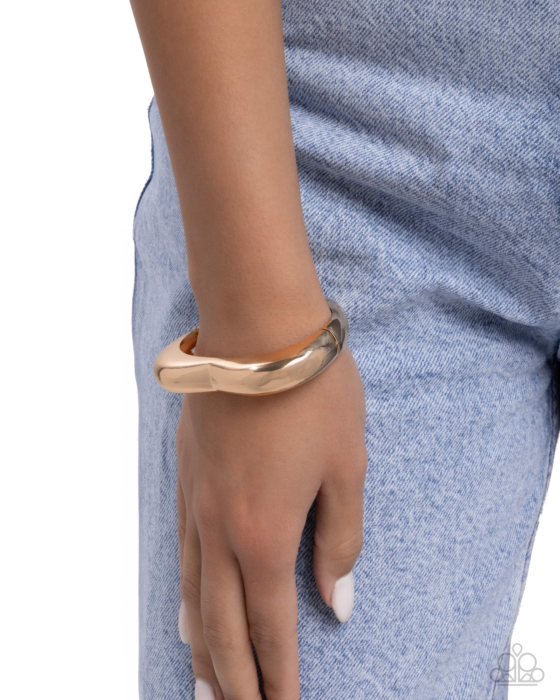 Gold bracelet on a wrist with a blue denim background