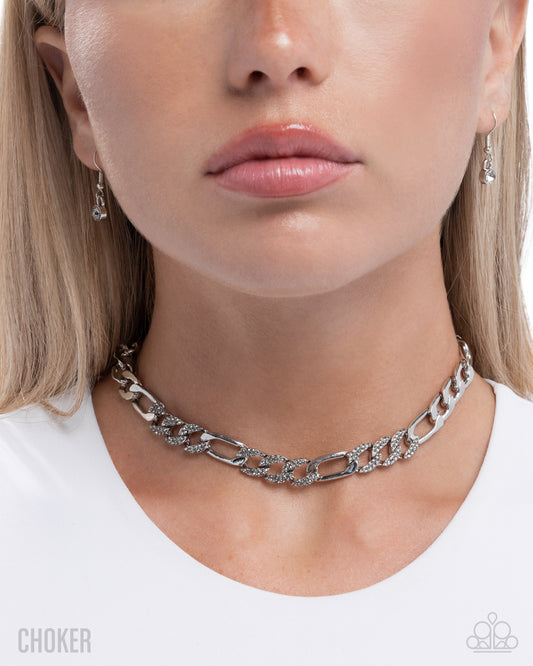 Close-up of a person wearing a silver chain choker necklace with earrings.