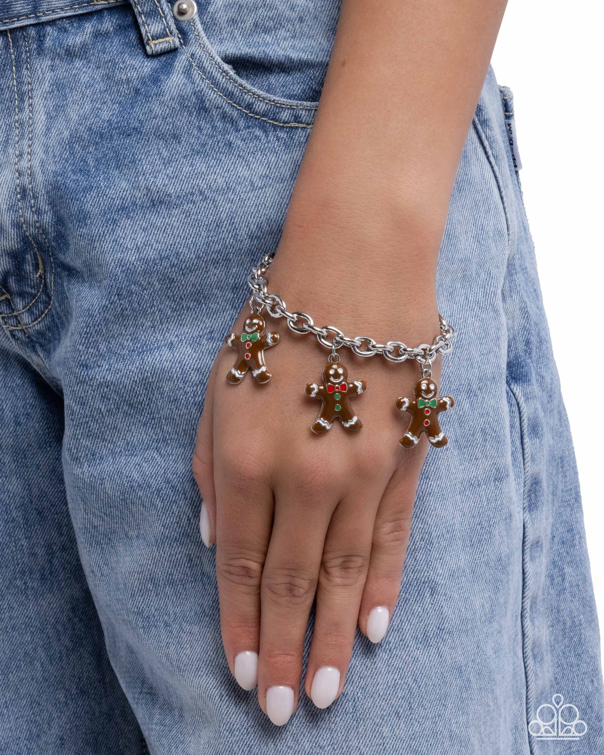 Hand wearing a silver bracelet with gingerbread man charms against a denim background