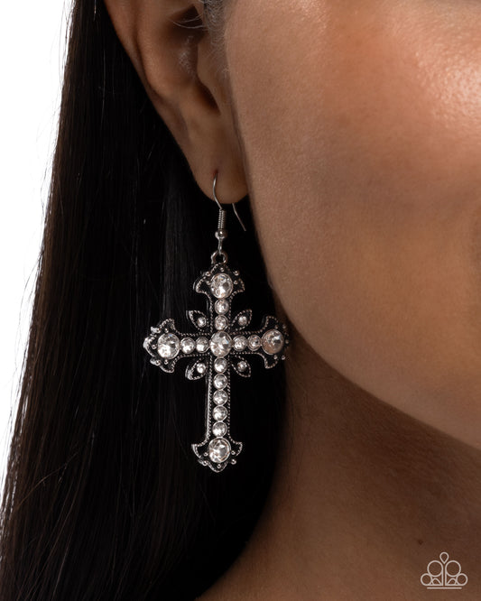 Silver cross earring worn by a person with dark hair on a white background