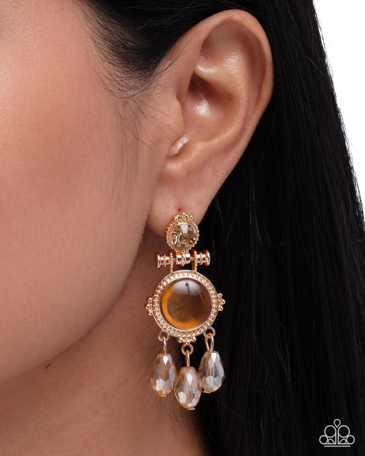 Gold earring with a brown gemstone worn by a person with dark hair.