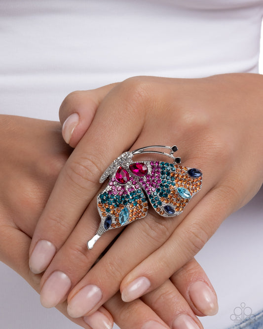Butterfly-shaped ring with colorful gemstones on a hand against a white background