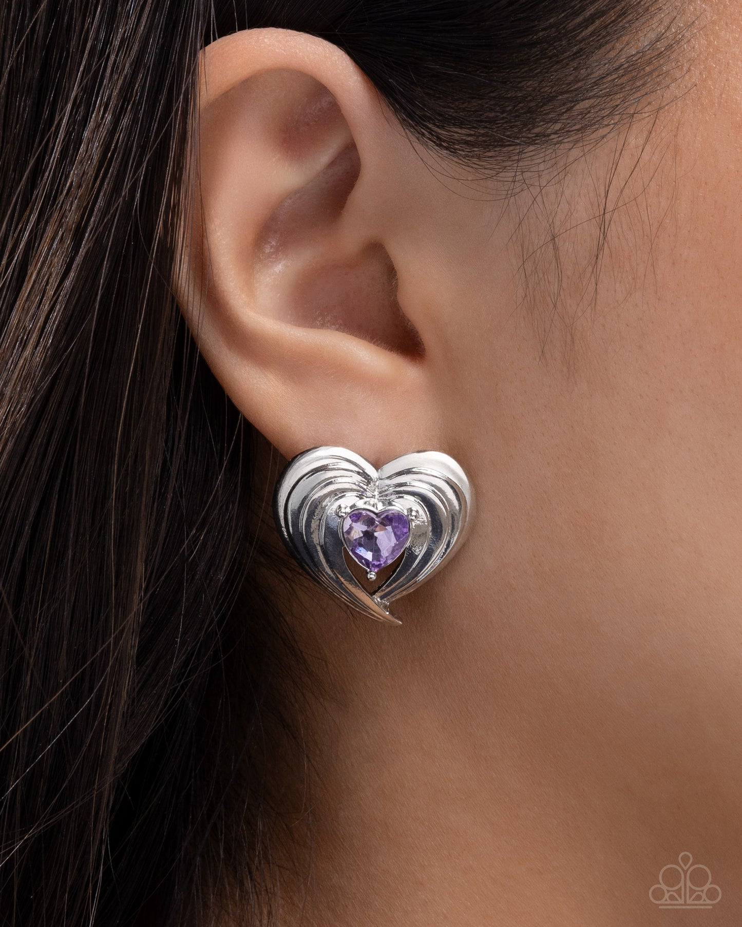 Heart-shaped earring with purple gemstone worn on an ear