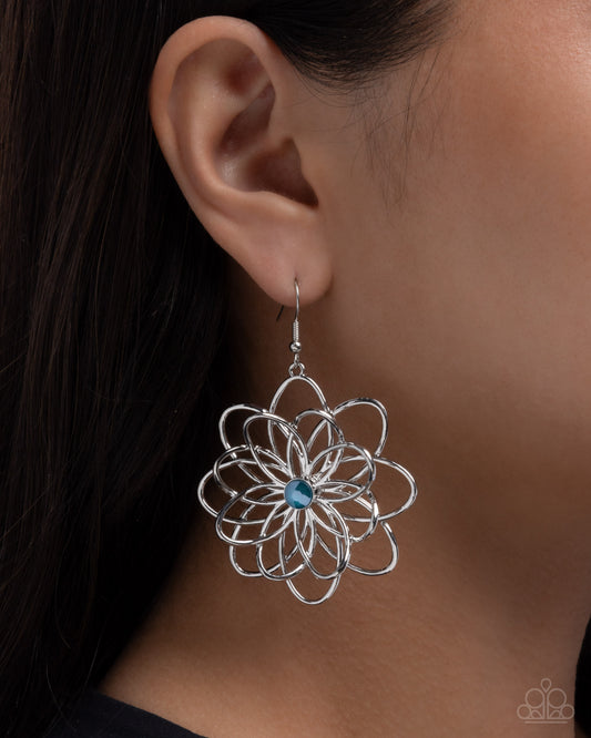 Silver floral earring with a blue gemstone worn by a person