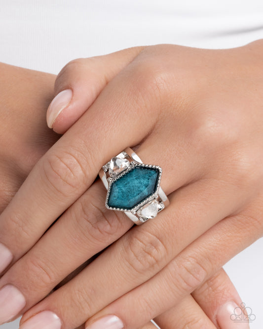 Silver ring with a blue gemstone on a hand against a white background