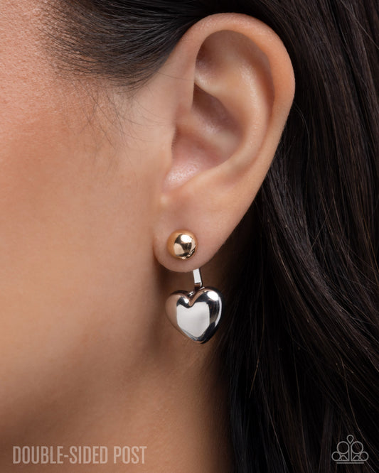 Close-up of an ear wearing a silver heart-shaped earring with a gold accent.
