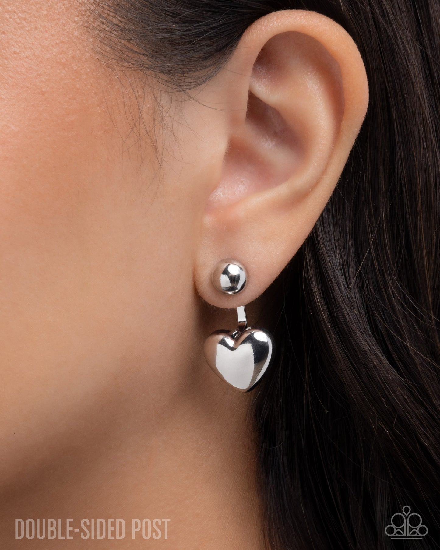 Silver heart-shaped earrings worn by a person with dark hair.