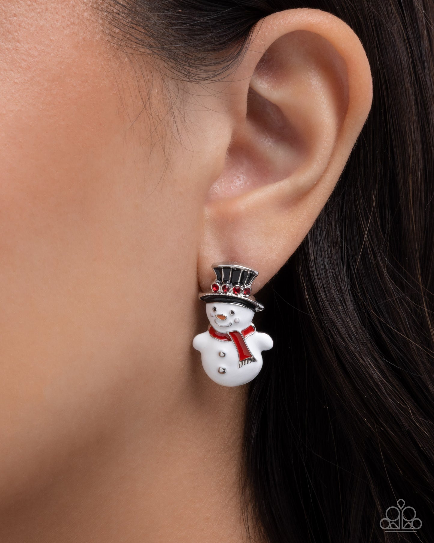 Snowman earring worn on an ear with a blurred background