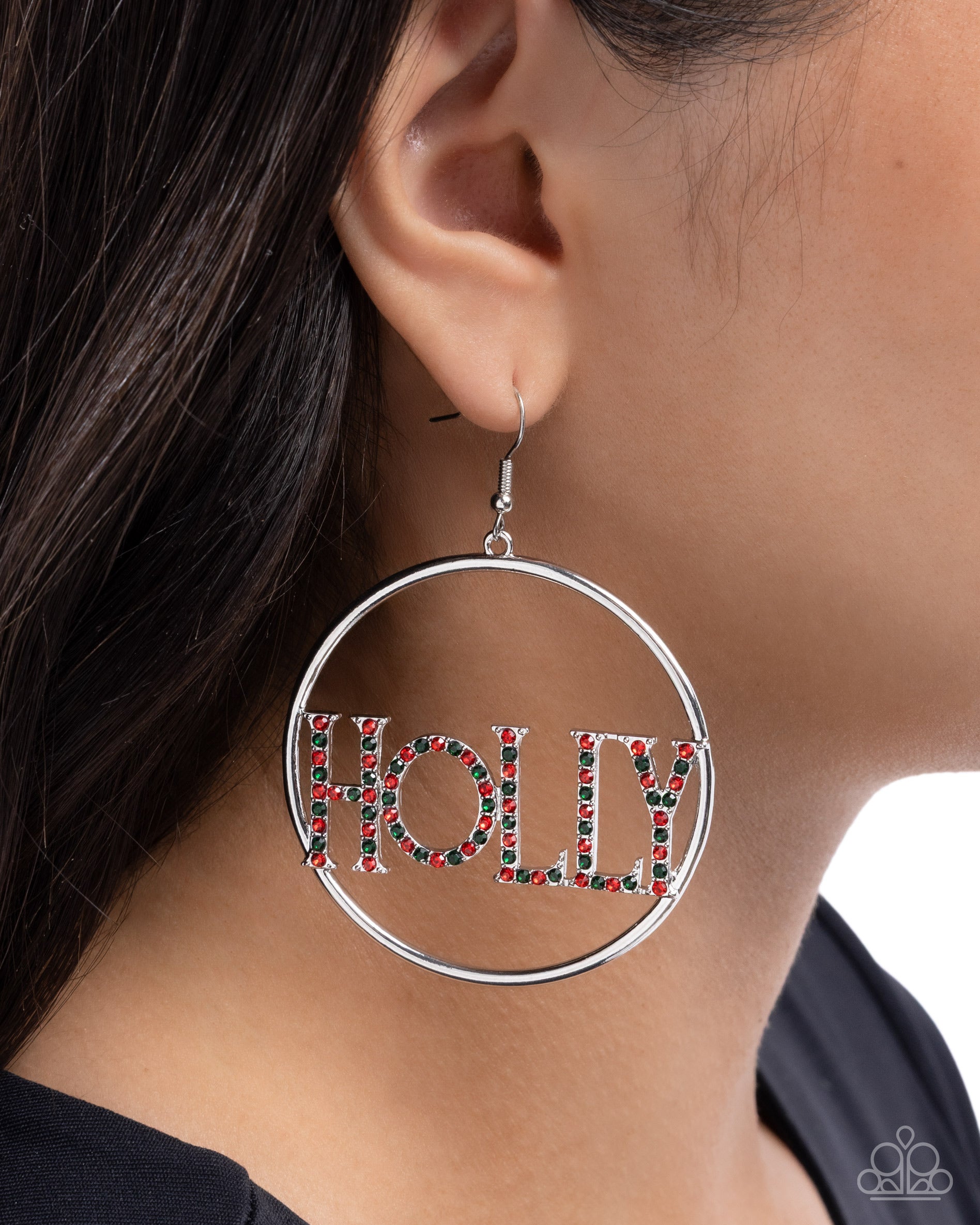 Silver hoop earring with 'HOLLY' text in red and green on a person wearing a black top.