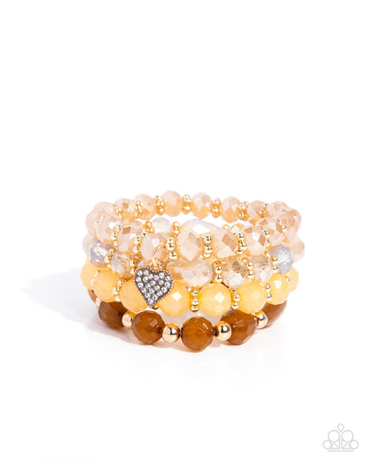 Stack of beaded bracelets with a heart charm on a white background