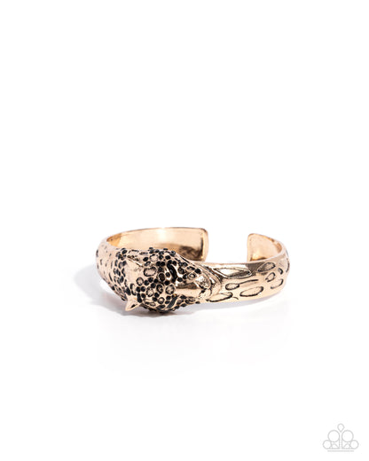 Gold and black patterned cuff bracelet on a white background