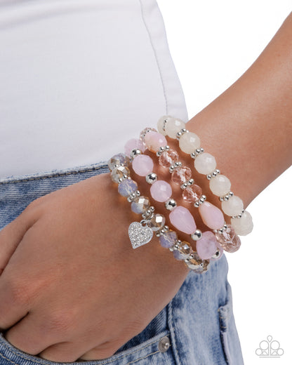 Stack of pink and silver beaded bracelets on a wrist with a white background