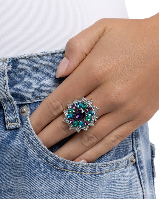 Hand wearing a decorative ring with gemstones, holding a denim jacket against a white background
