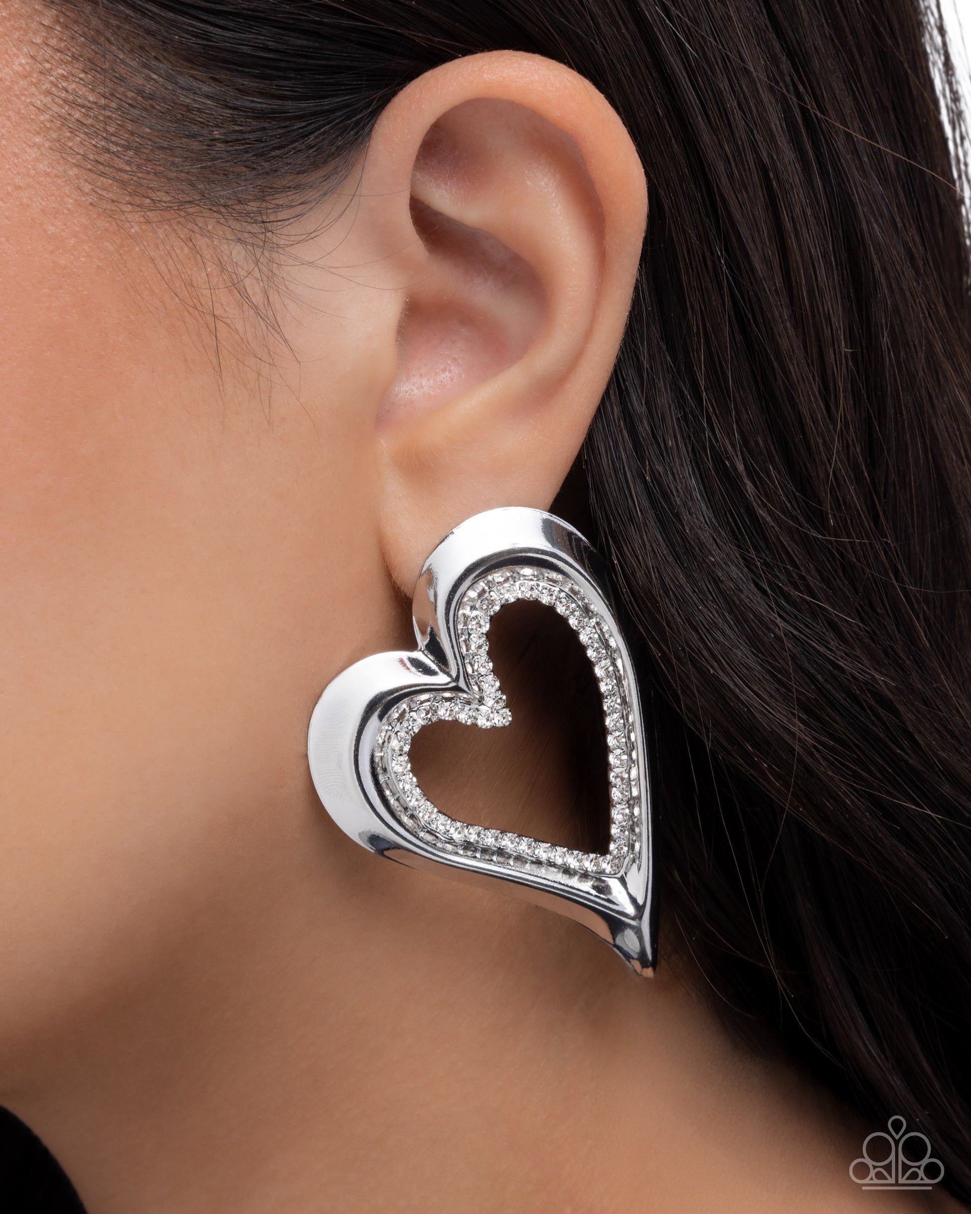 Heart-shaped silver earring worn by a person with dark hair.