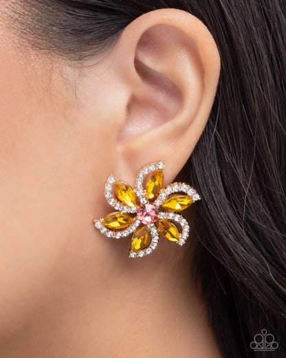 A close-up of a model's ear wearing a flower-shaped earring with yellow marquise-cut crystals, a pink center stone, and clear rhinestone borders.