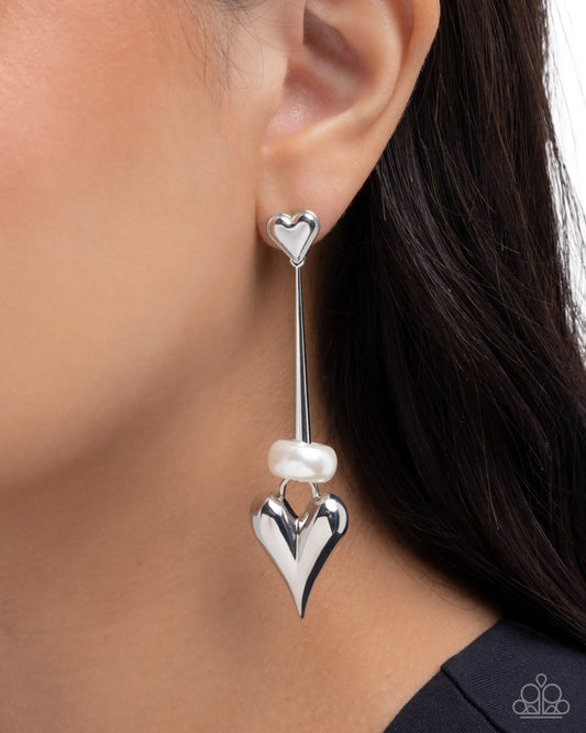 Silver heart-shaped earrings with a pearl on an ear against a blurred background