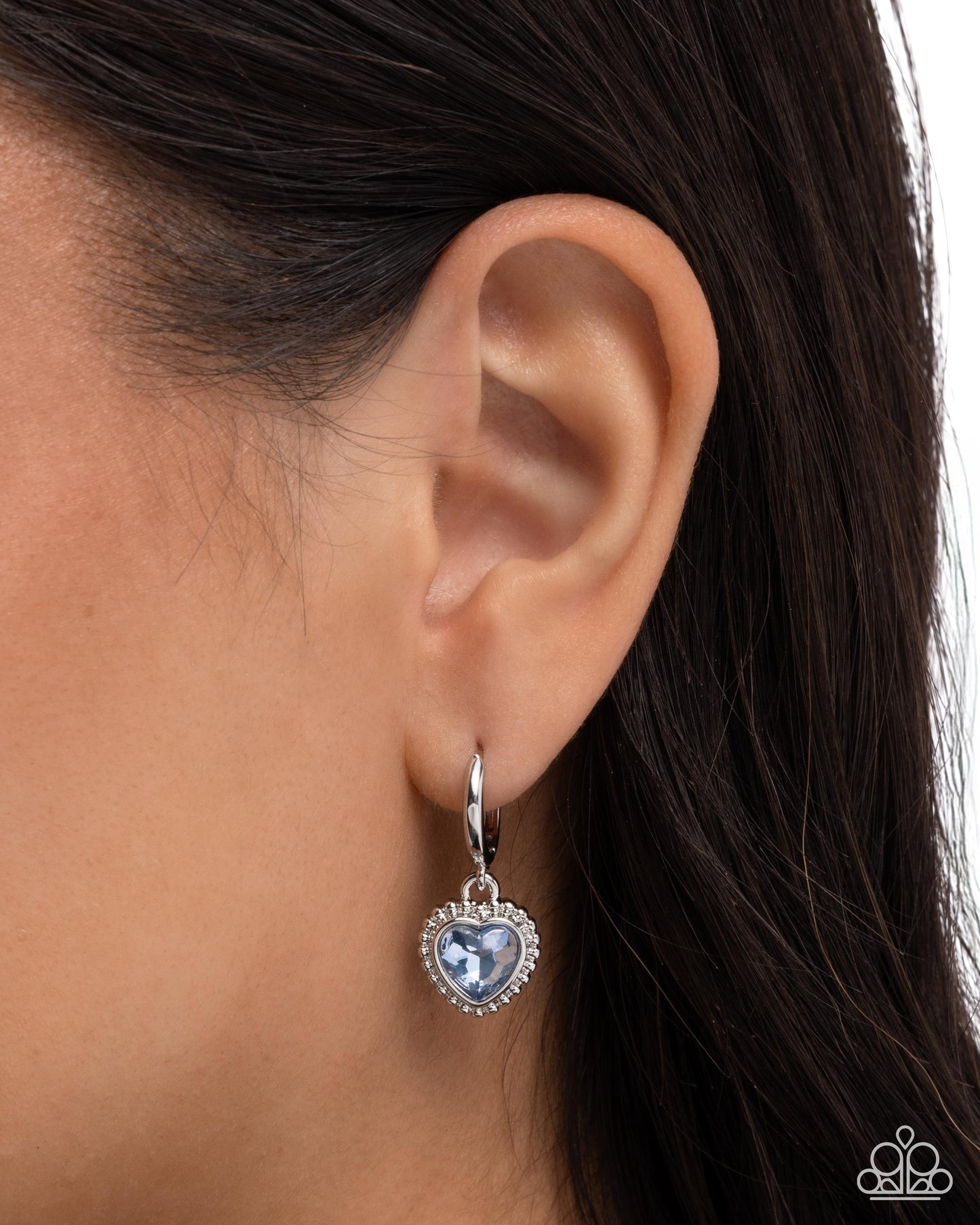 Heart-shaped earring with blue gemstone worn by a person