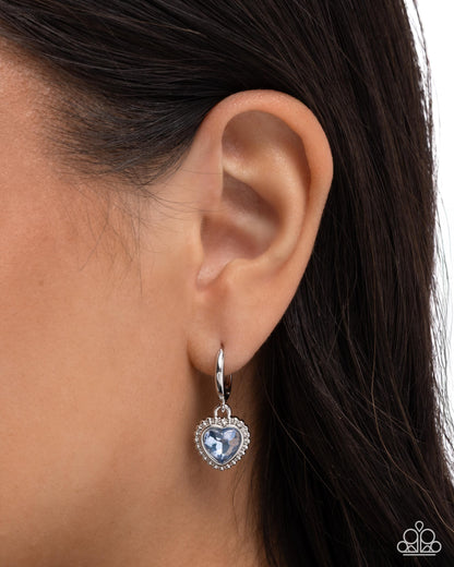 Heart-shaped earring with blue gemstone worn by a person