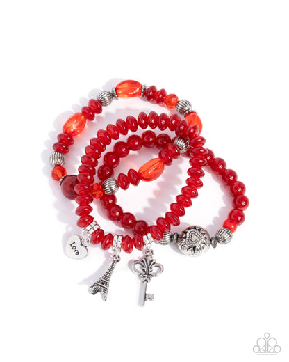 Red beaded bracelet with silver charms on a white background