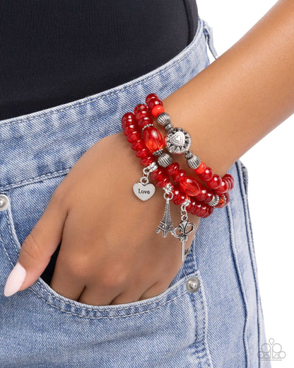 Red beaded bracelet with silver charms on a wrist against a denim background