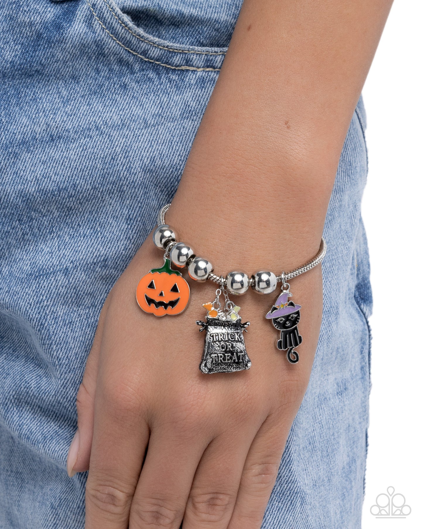 Bracelet with Halloween-themed charms on a wrist against a denim background
