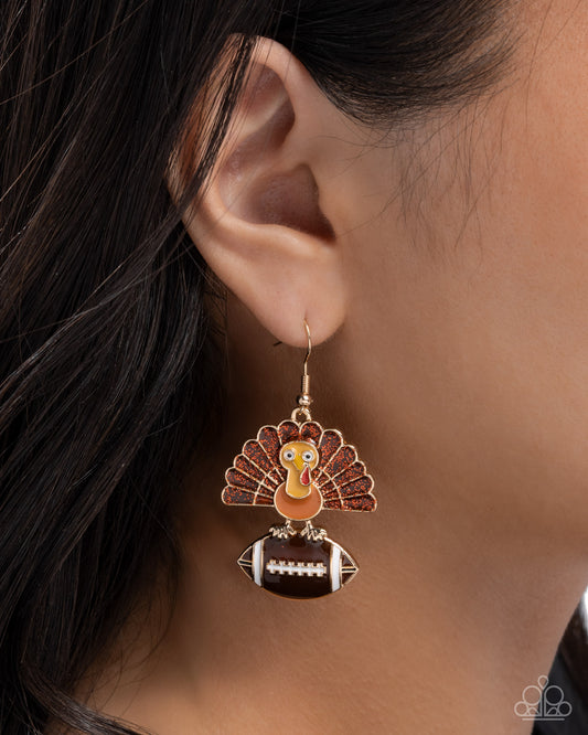 Earring with a turkey design on a football, worn by a person.