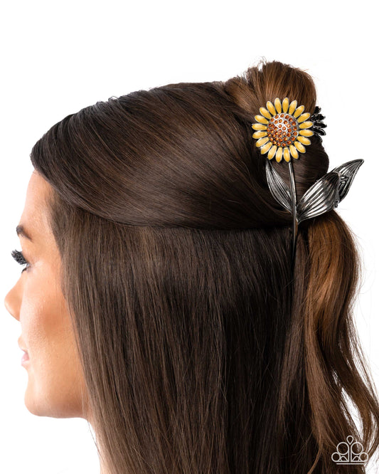Woman with brown hair styled with a decorative hair accessory featuring a sunflower design.