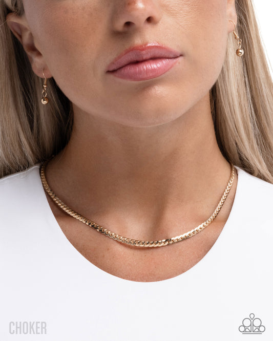 Close-up of a person wearing a gold choker necklace with matching earrings.