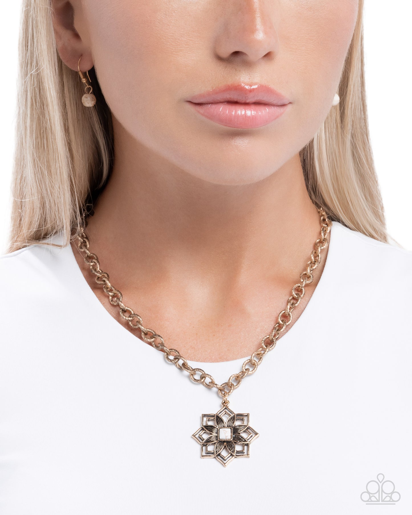 A close-up of a model wearing a gold chain necklace with a geometric starburst pendant, styled with a white top against a clean white background.