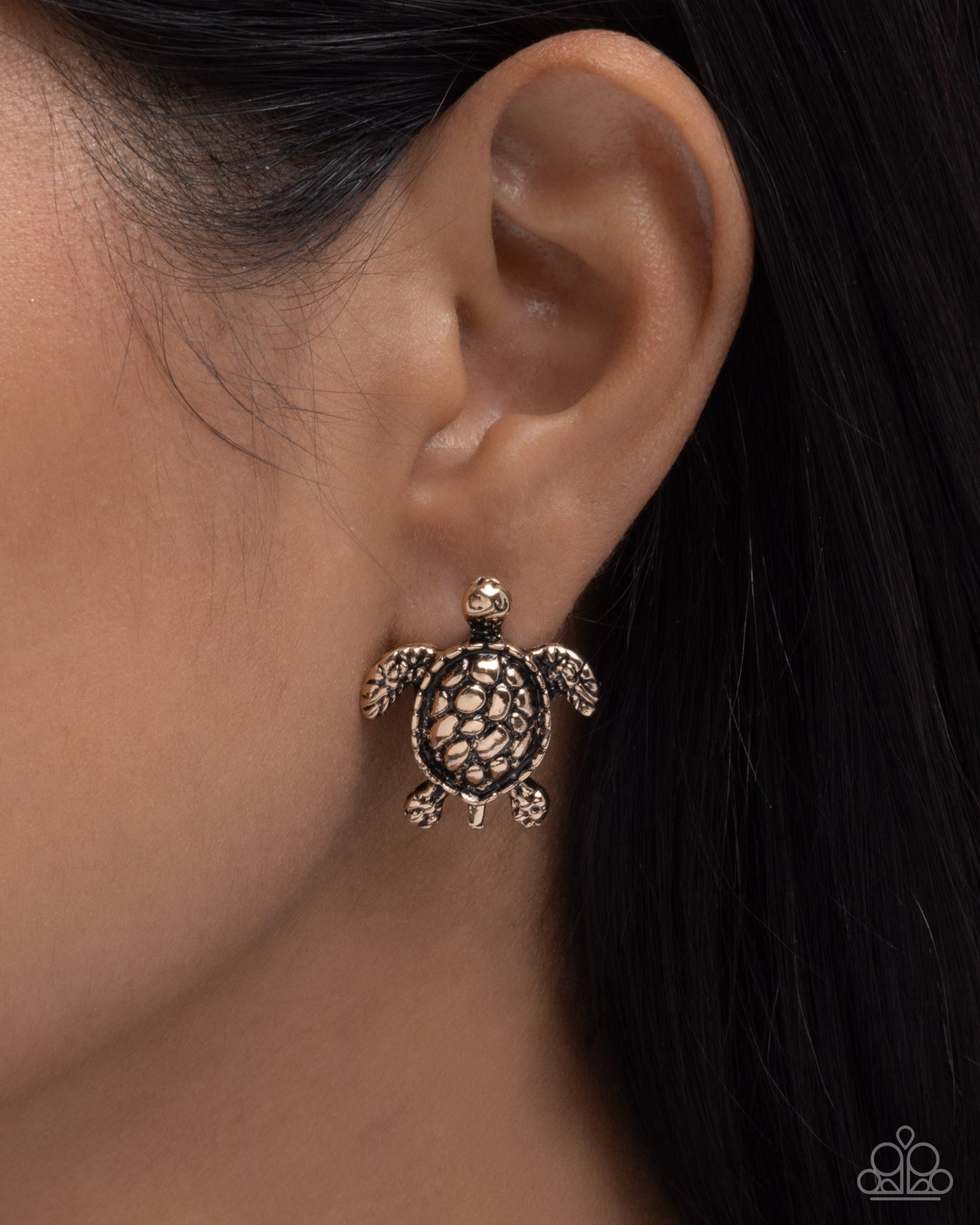 Close-up of an ear wearing a turtle-shaped earring with a dark background