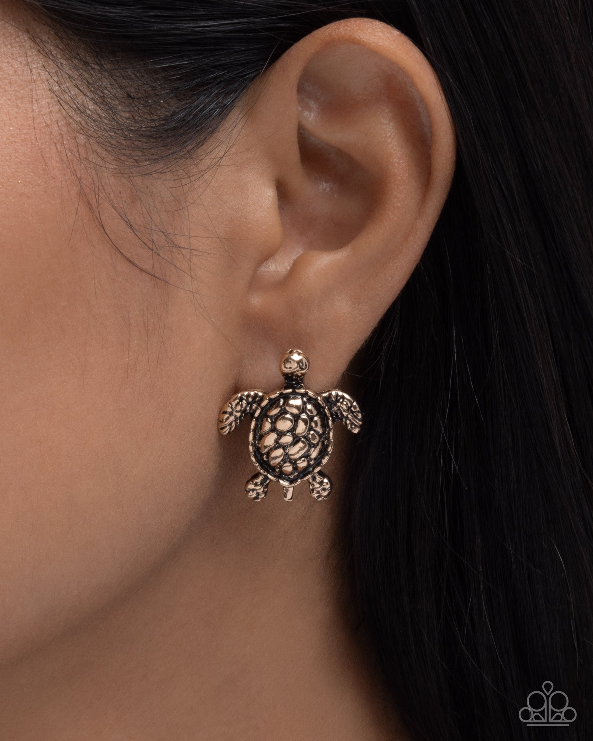 Close-up of an ear wearing a turtle-shaped earring with a dark background