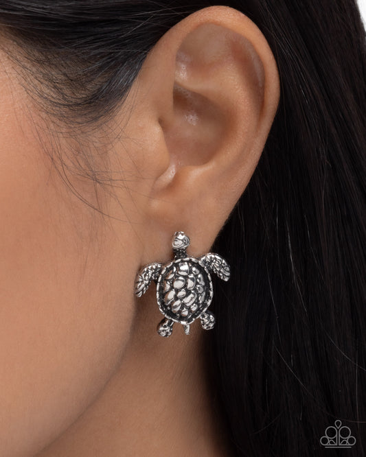 Silver turtle earring worn by a person with dark hair.