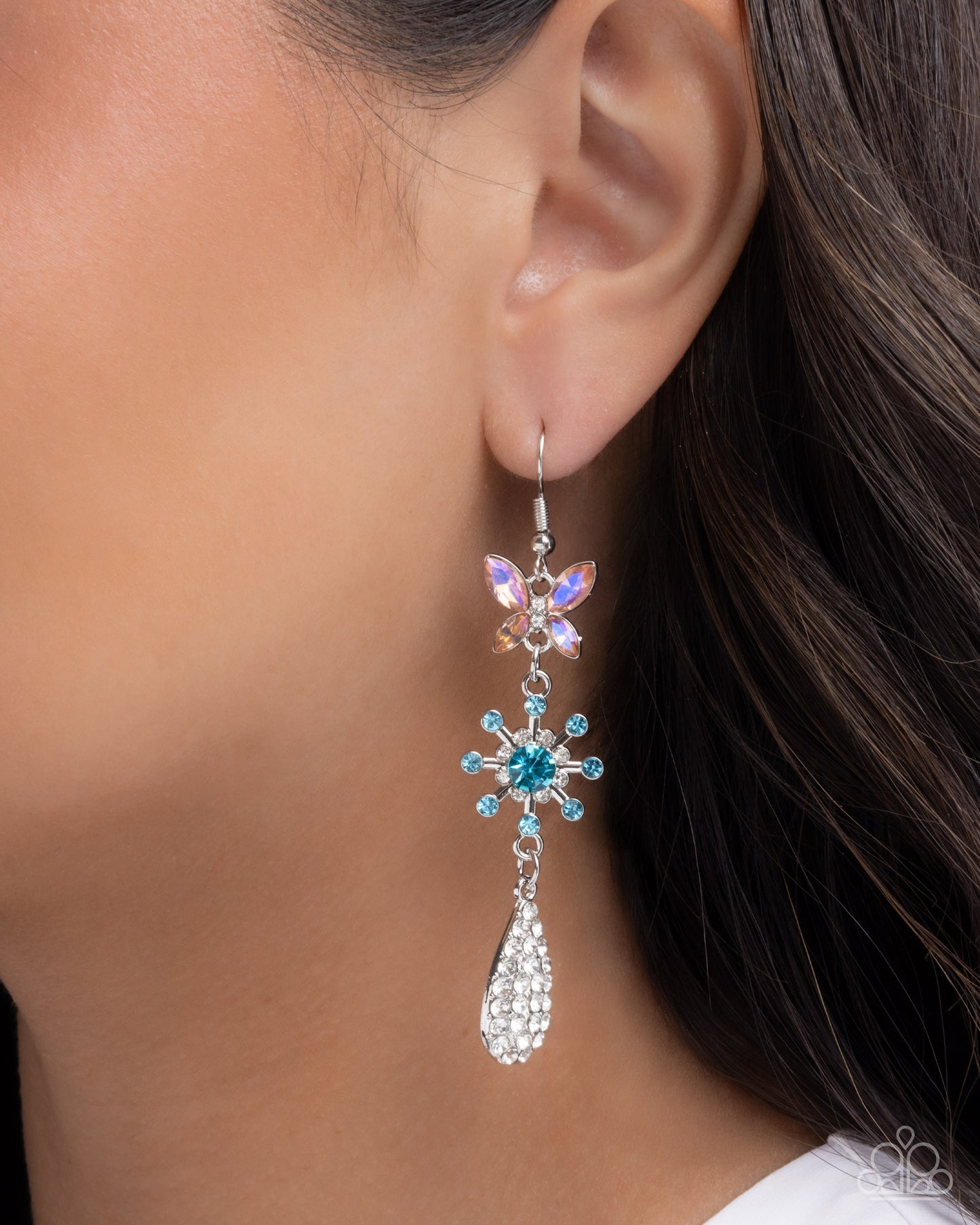 Close-up of an ear wearing a decorative earring with a blue gemstone.