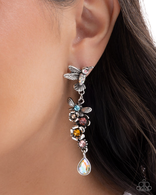 Close-up of an ear wearing a colorful bee-themed earring with gemstones.