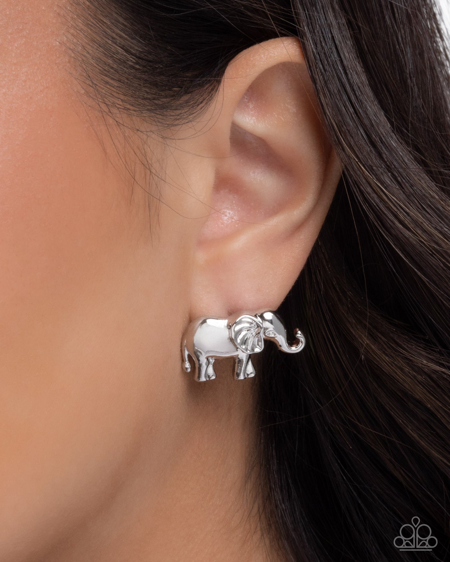 Silver elephant earring worn on an ear with dark hair.
